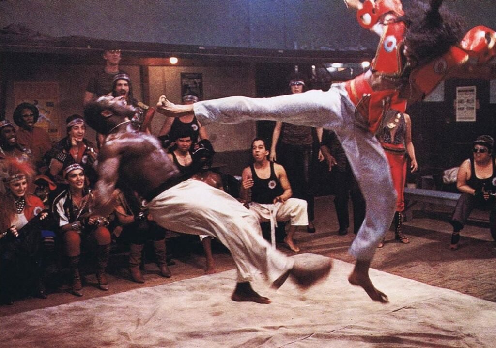 “Sho’nuff em ação: o ‘Shogun do Harlem’ exibe seu golpe aéreo em uma das cenas mais icônicas de The Last Dragon (1985), diante de uma plateia vibrante e estilosa dos anos 80.”